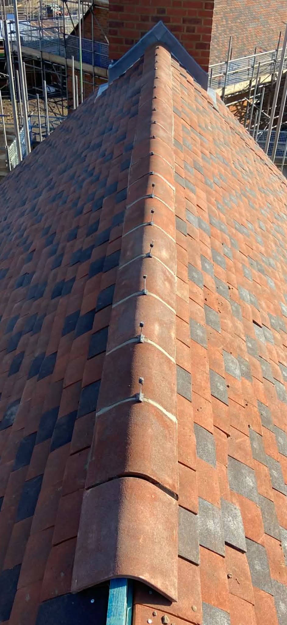 A clay tiled hip with a mechanically fixed ridge, seen against a blue sky