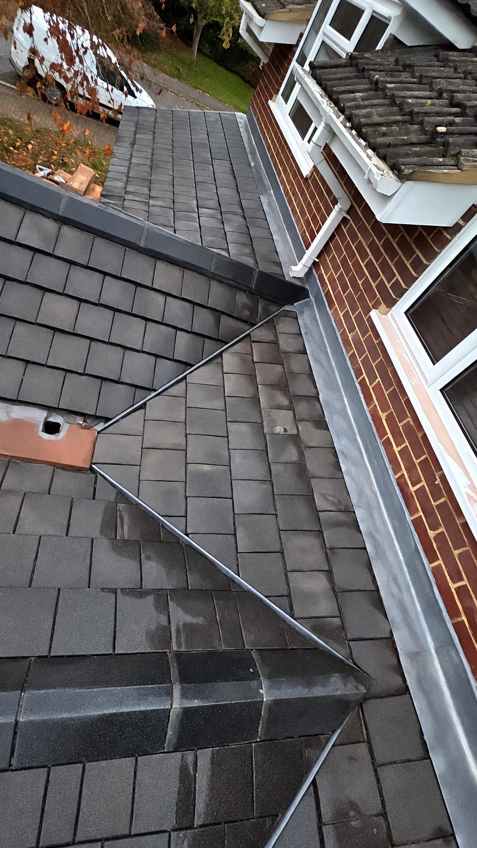 A slate roof with dressed lead valleys running down to a red brick wall