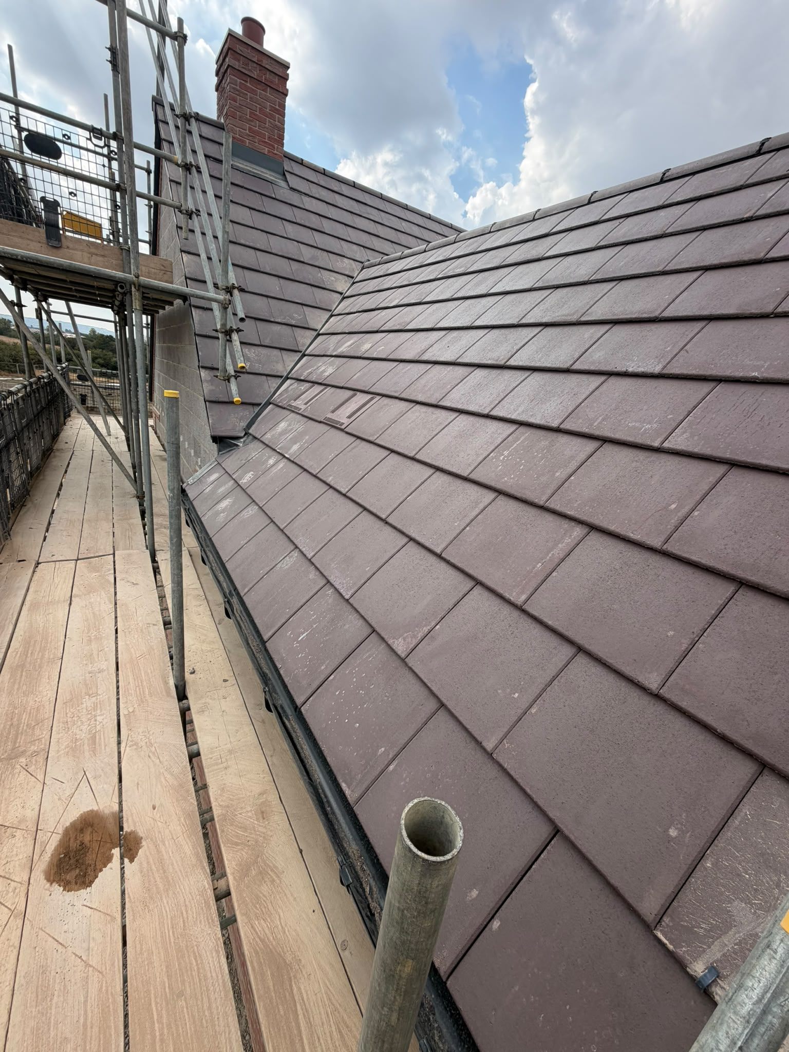 An interlocking tile roof with a neat dry-fixed hip, scaffold alongside